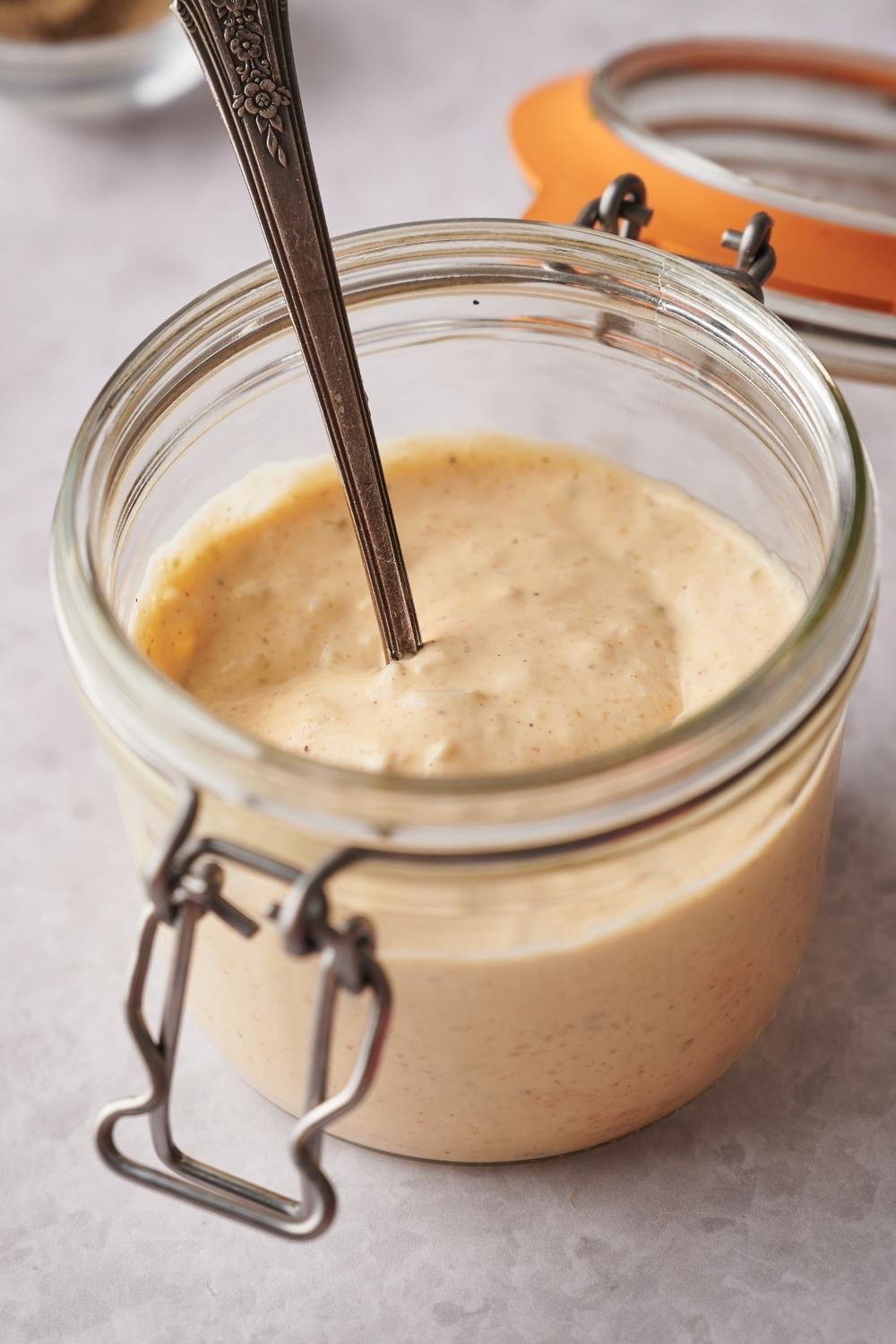 A small mason jar with homemade big Mac sauce and a spoon in it.