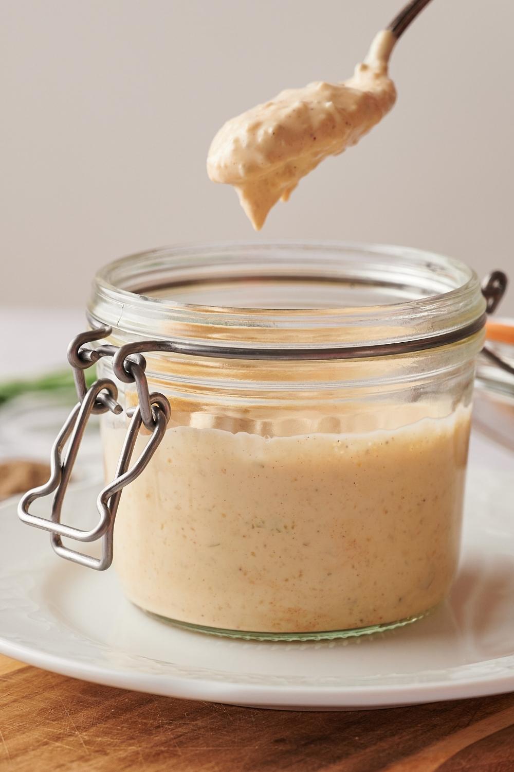 A small mason jar with a lid containing homemade big Mac sauce. A spoon has scooped some and has it suspended over the mason jar.