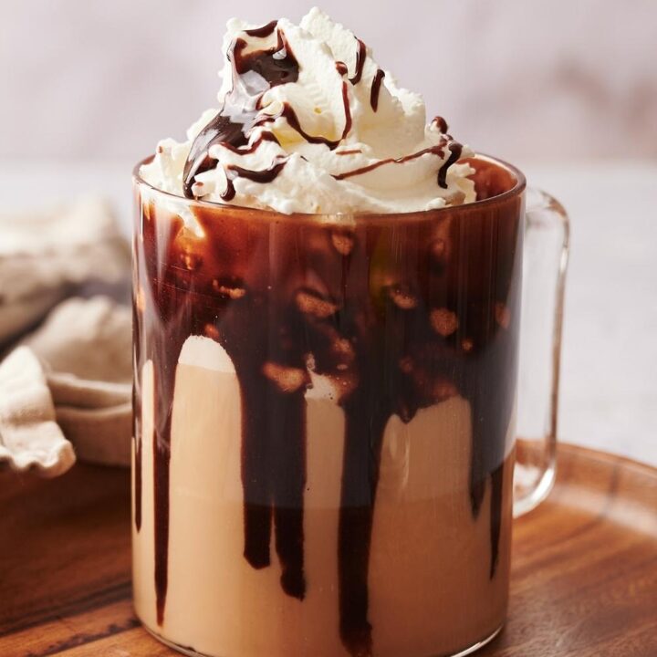 A clear glass mug with a homemade starbucks cafe mocha topped with whipped cream and chocolate syrup drizzled on top.