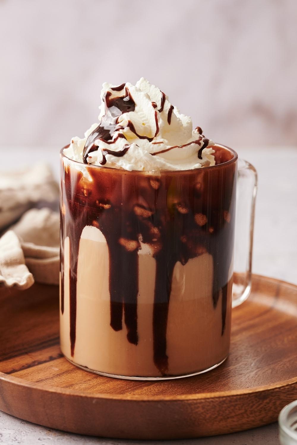 A clear glass mug with a homemade starbucks cafe mocha topped with whipped cream and chocolate syrup drizzled on top.