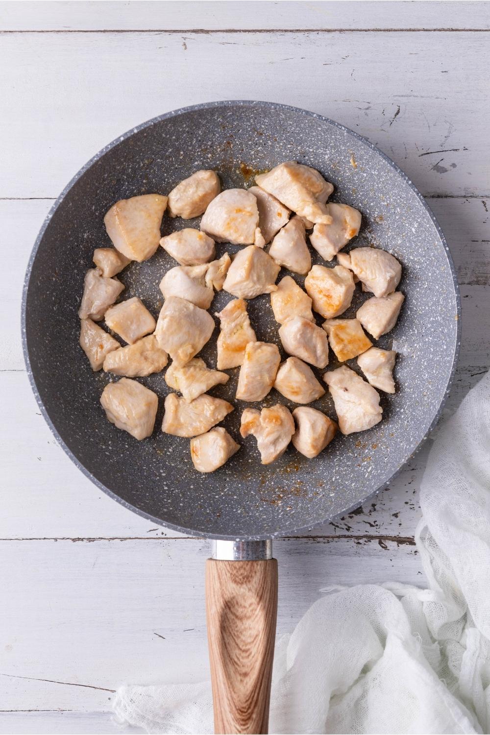 Skillet with cooked chicken breast cut into chunks.