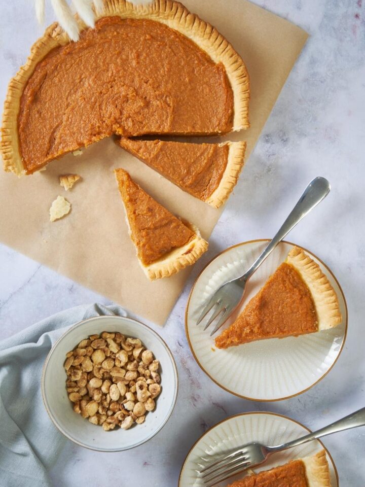 Patti Labelle's sweet potato pie has been sliced into individual servings, two of which are on small white plates. A bowl of chopped nuts is next to the pie.