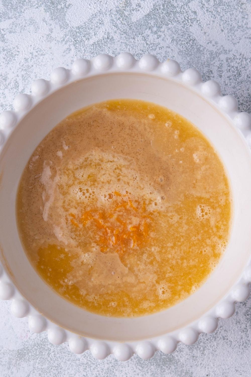 A mixing bowl with creamed butter, sugar and egg. Orange juice has just been added to the bowl.