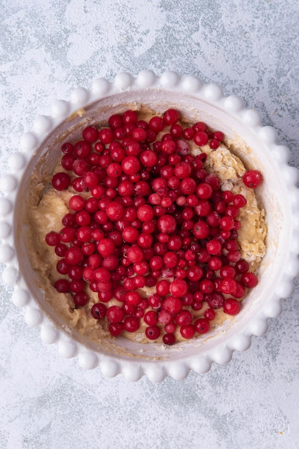 A mixing bowl with bread batter in it, the fresh cranberries have just been added to the bowl.