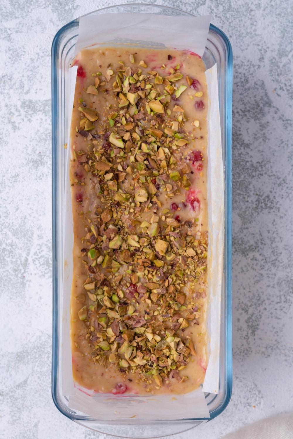 A loaf pan with the cranberry nut bread batter topped with chopped pistachios.