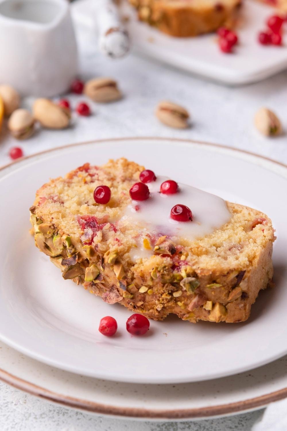 A slice of cranberry nut bread on a serving plate. It is glazed and has a few fresh cranberries to garnish.