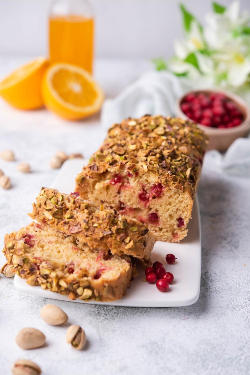 Two slices of cranberry bread in front of a loaf of cranberry bread on a white plate.