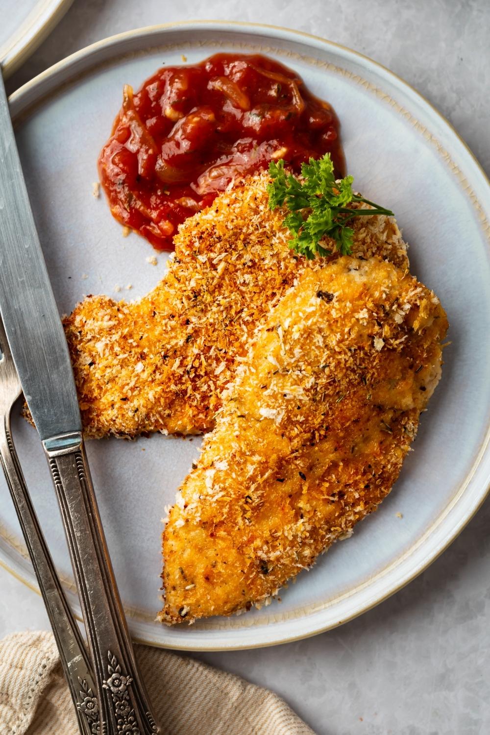 top shot of two panko chicken pieces with a side of marinara sauce. a fork and knife sit on the plate