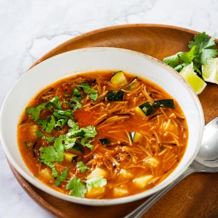 a bowl of fideo soup with lime wedges and cilantro