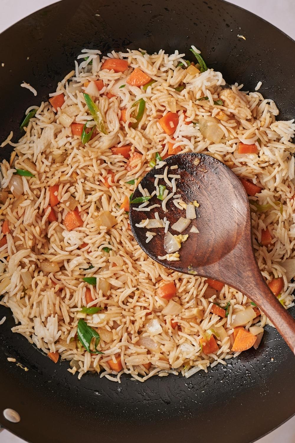 A wooden spoon in a wok that is filled with rice and veggies.