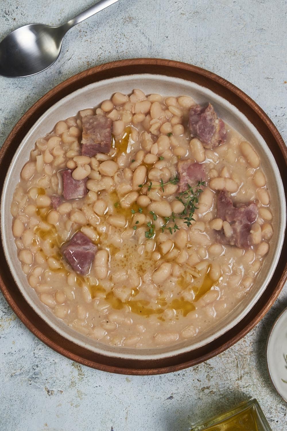 A big bowl of great northern beans with ham served on a wooden plate tray.