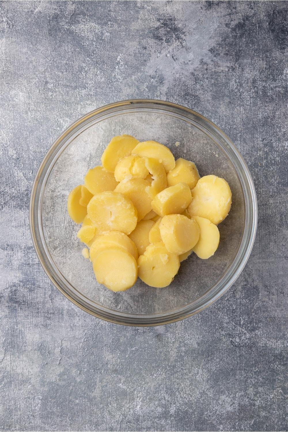 Clear bowl with cooked and peeled Russet potatoes cut into thick slices.