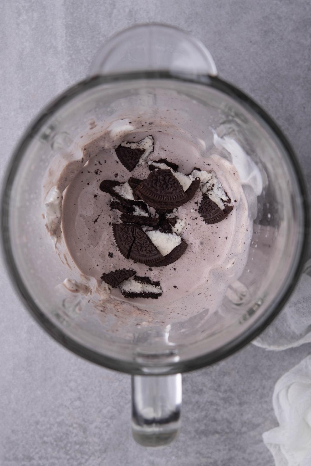 A blender with the ice cream mixture in it. Large oreo chunks have just been addd to it.