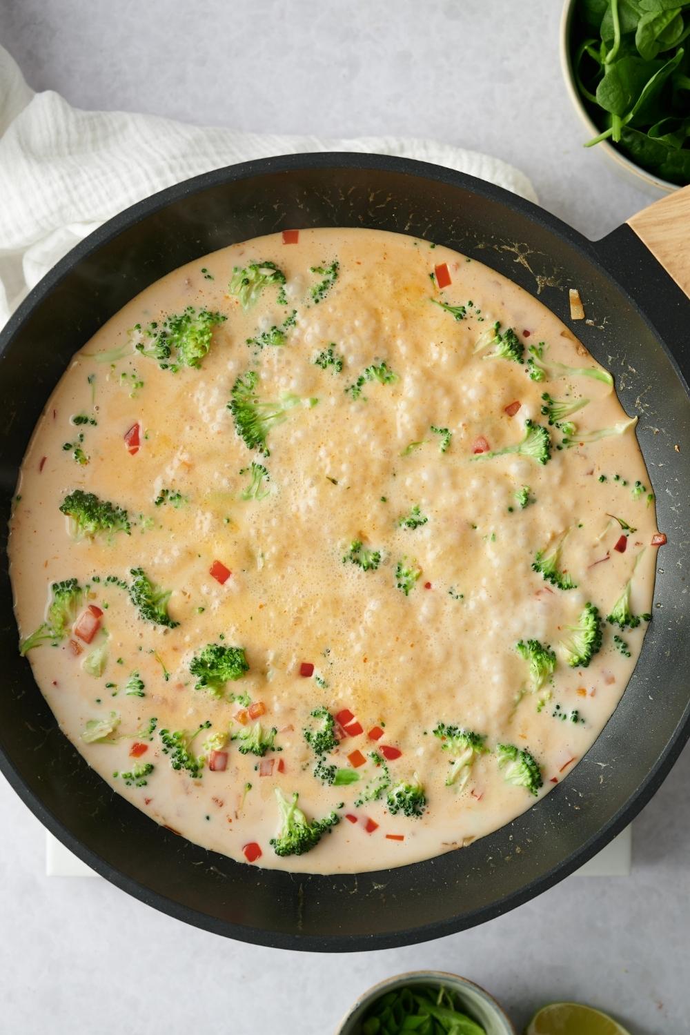 A pan with veggies and curry cream sauce being reduced.