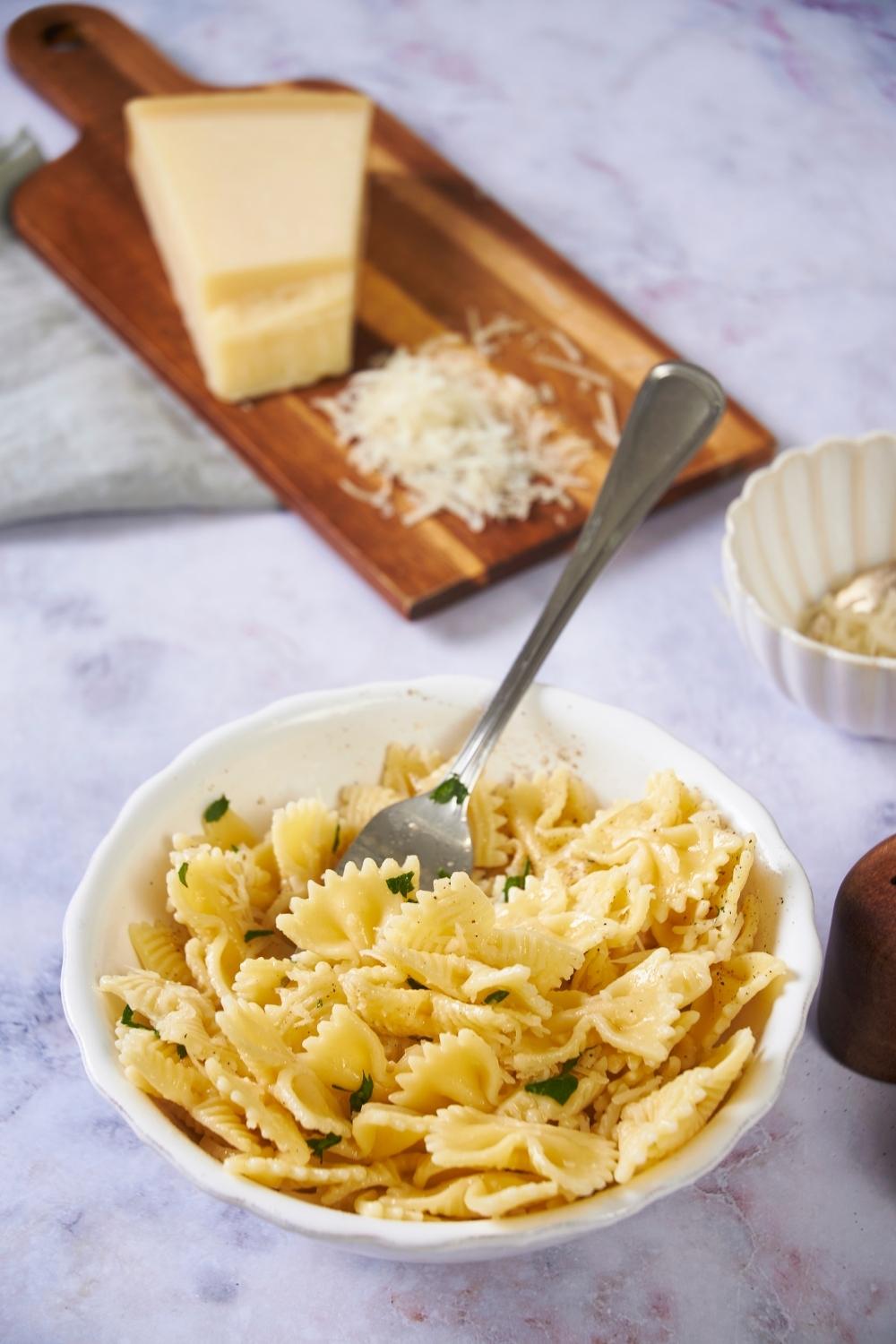 Microwaved pasta in a white bowl with a fork in the bowl, next to a block of grated parmesan cheese on a wood board.