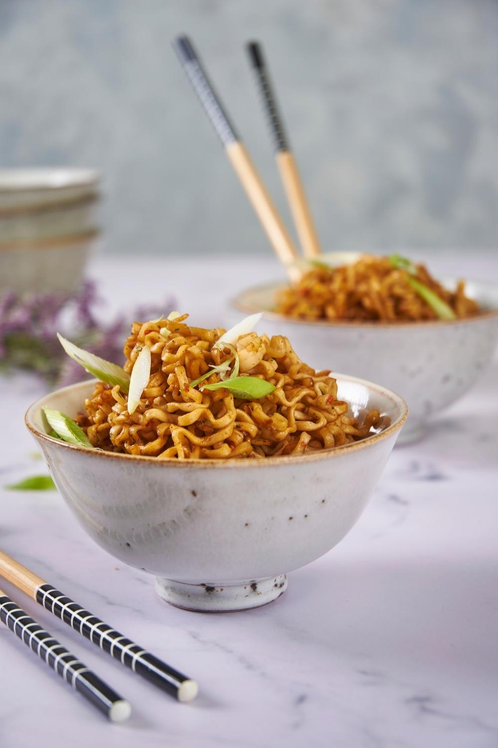 Two bowls of microwaved ramen, one with chopsticks in the bowl and one with chopsticks next to the bowl, both garnished with green onion.