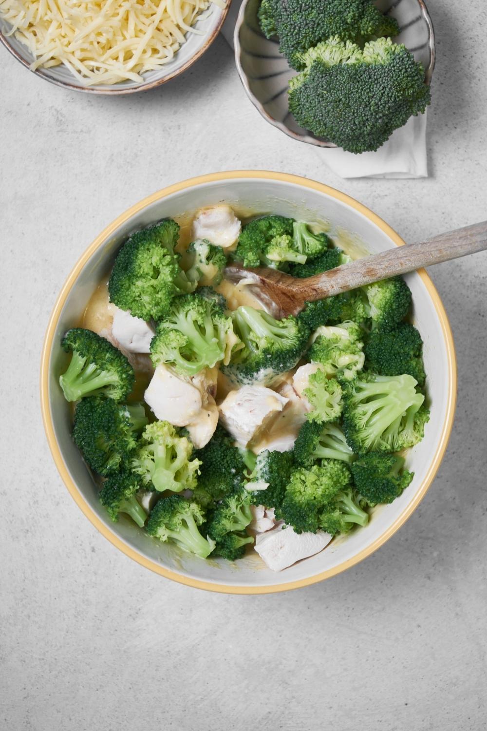 top view of a large mixing bowl filled with broccoli, sour cream, and condensed soup. a wooden spoon sits on top.