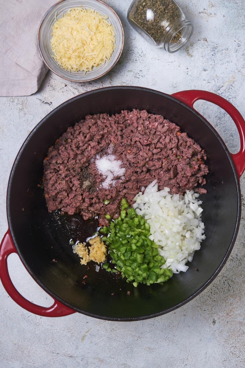 A pot that has ground beef, onions, gralic, and diced green pepper in it.