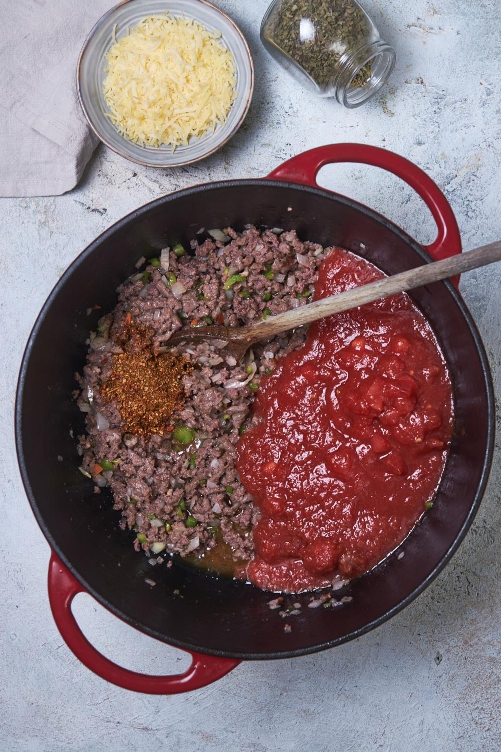 A pot that is filled half with crushed tomatoes and half with ground beef.