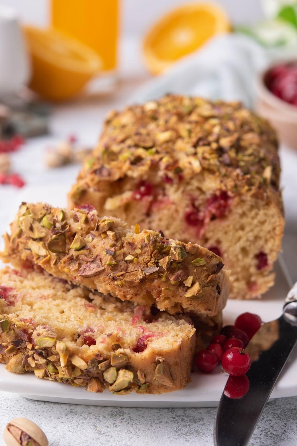 A plate with a loaf of cranberry walnut bread. Two slices lay piled on top of one another. Fresh cranberries garnish the plate.