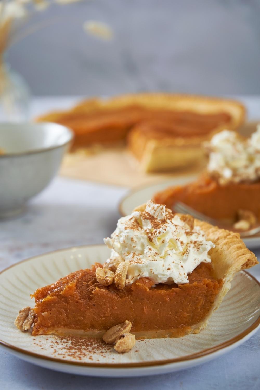 Patti Labelle's sweet potato pie served on a white plate, in the background there is the rest of the pie.