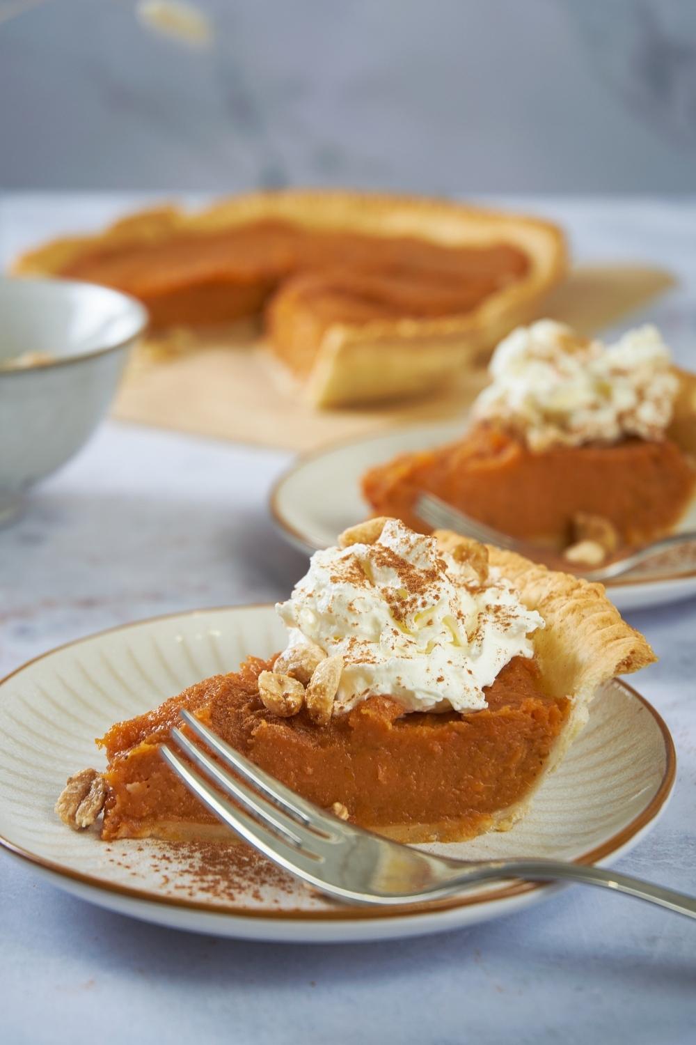 Patti Labelle's sweet potato pie served on a white plate with a fork on the plate, in the background there is the rest of the pie.