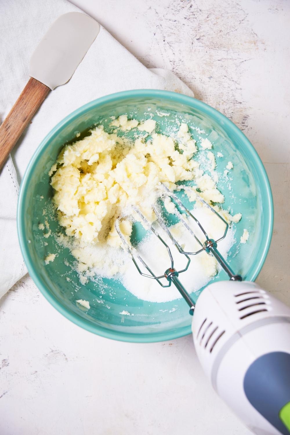 butter and sugar in a large teal bowl being beaten together with a mixer