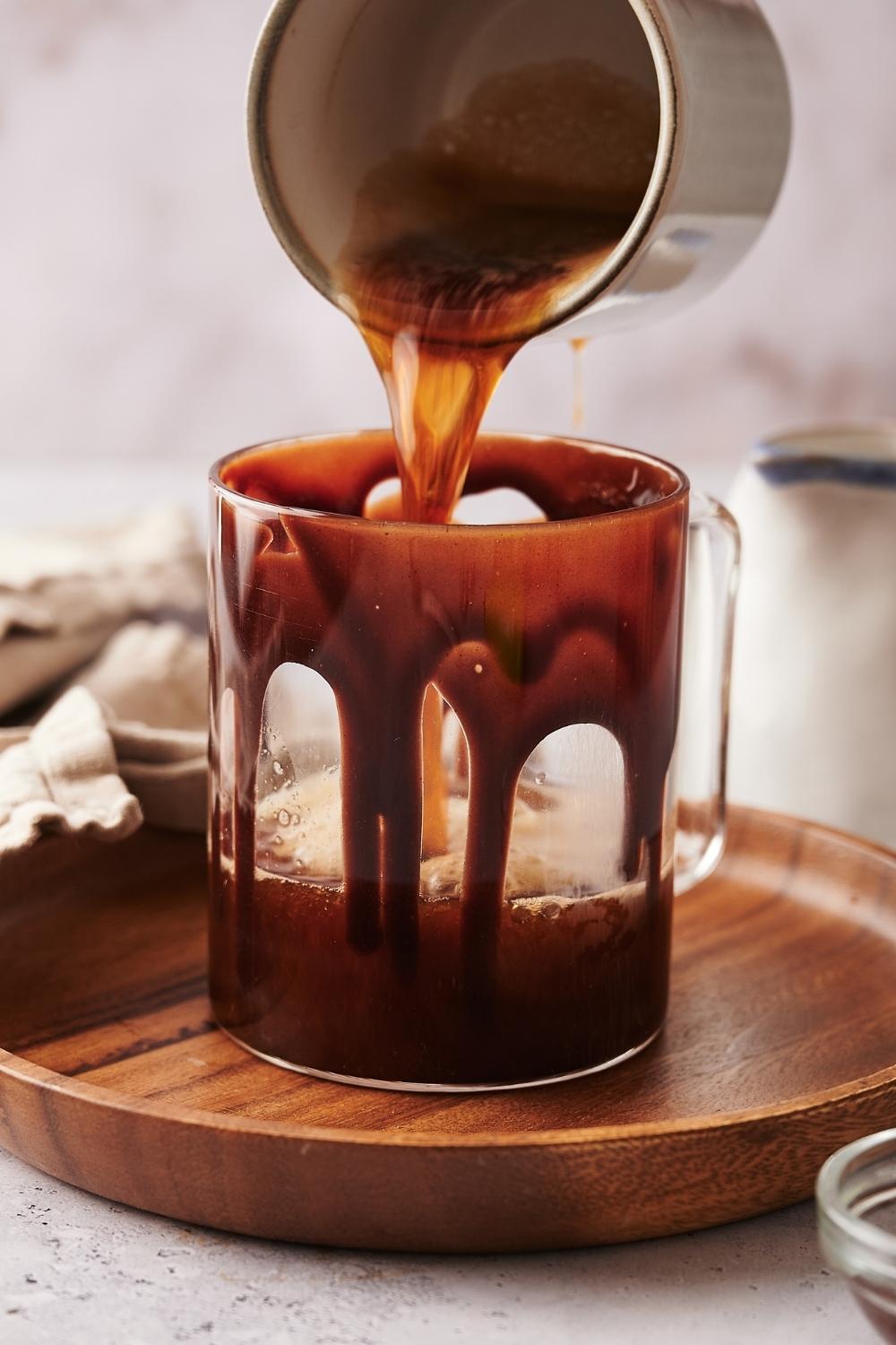 A cup pouring espresso into a glass mug that is lined with chocolate sauce.