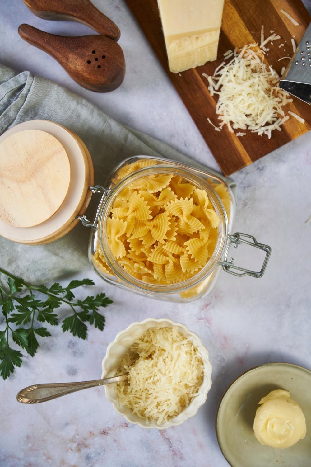 An assortment of ingredients for microwaving pasta including a jar of uncooked pasta, parmesan cheese, butter, and parsley.