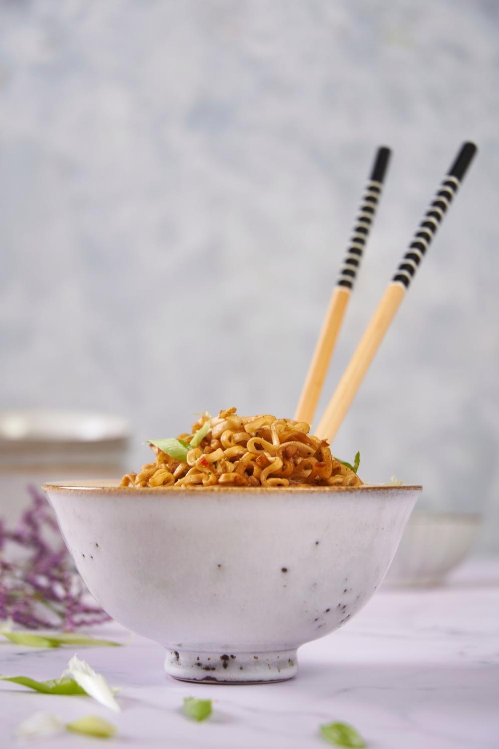 Microwaved ramen in a white bowl with a set of chopsticks in the bowl.