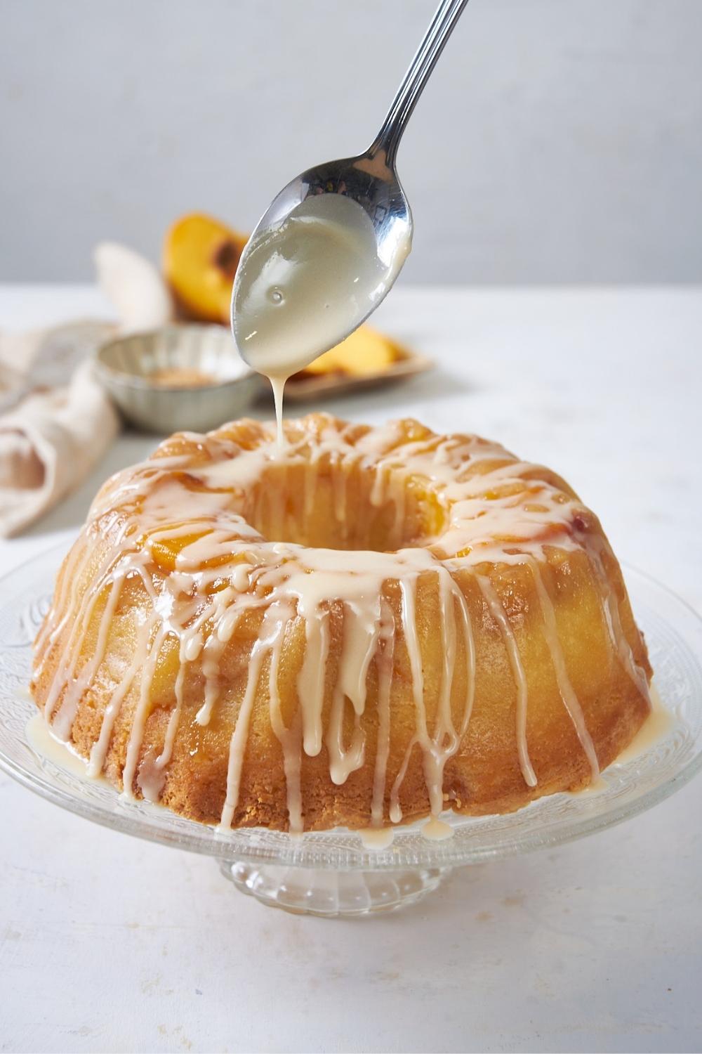 A spoon drizzling icing on top of a peach cobbler bundt cake.