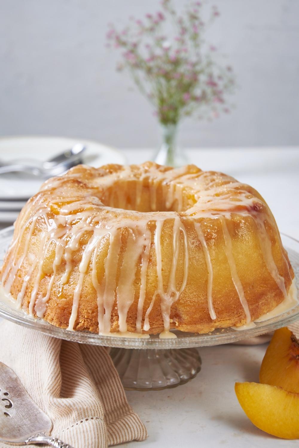 A peach cobbler bundt cake drizzled with glaze on a cake stand.