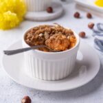 Sweet potato souffle in a ramekin on a white plate with a spoon in the souffle and a bite taken out.