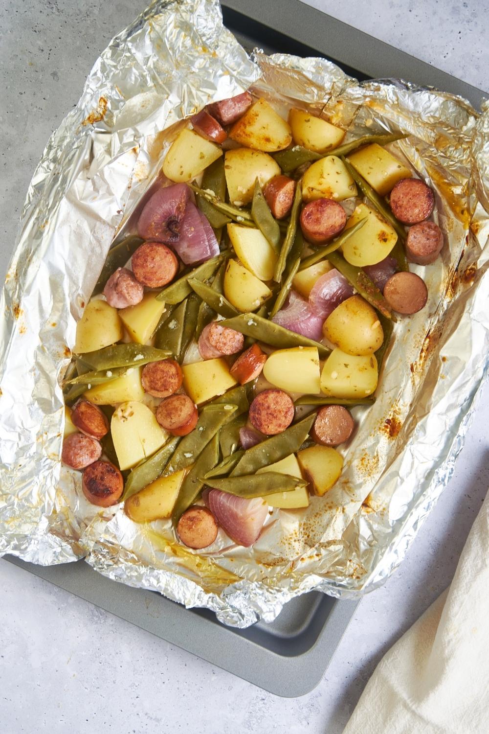 Freshly baked sausage and green bean casserole in a baking dish lined with foil.