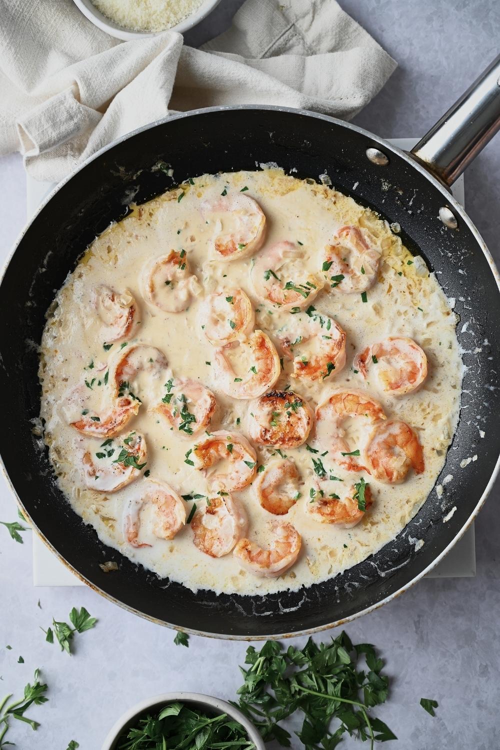 A pan with onion, garlic, and shrimp with garlic cream sauce reducing.