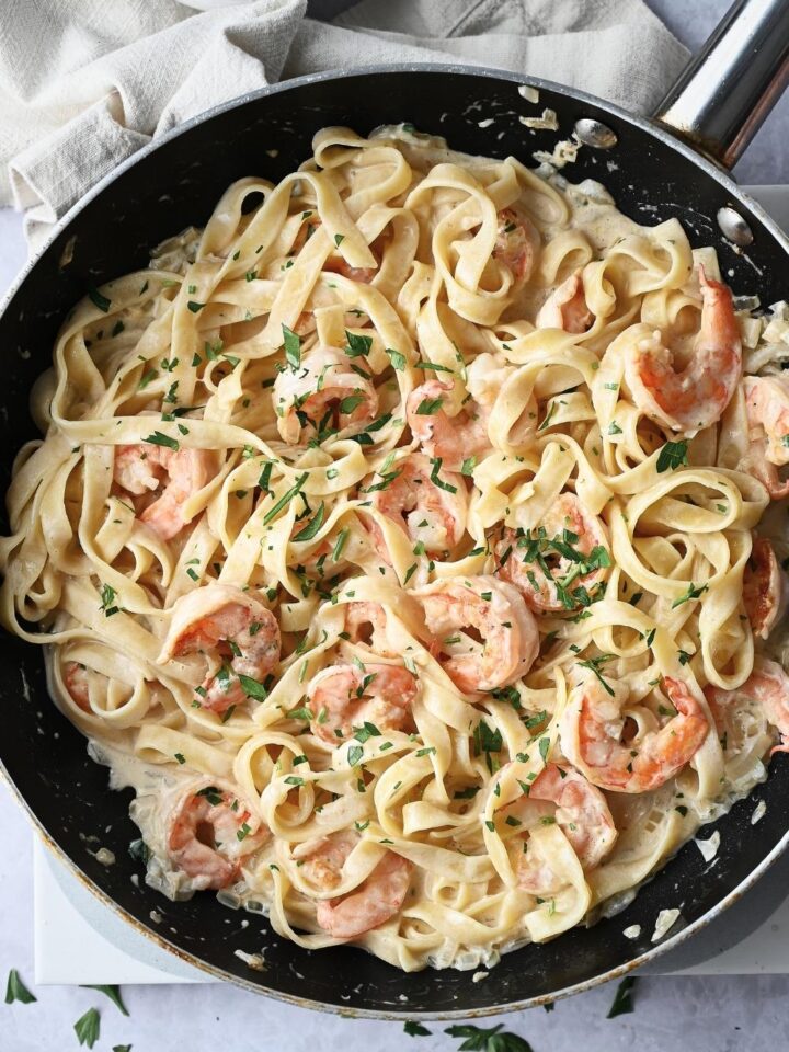 A pan with homemade pasta shrimp with fettuccine noodles garnished with parsley and parmesan cheese.