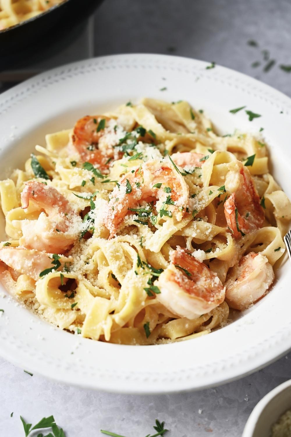 A serving bowl with homemade pasta shrimp with fettuccine noodles garnished with parsley and parmesan cheese.