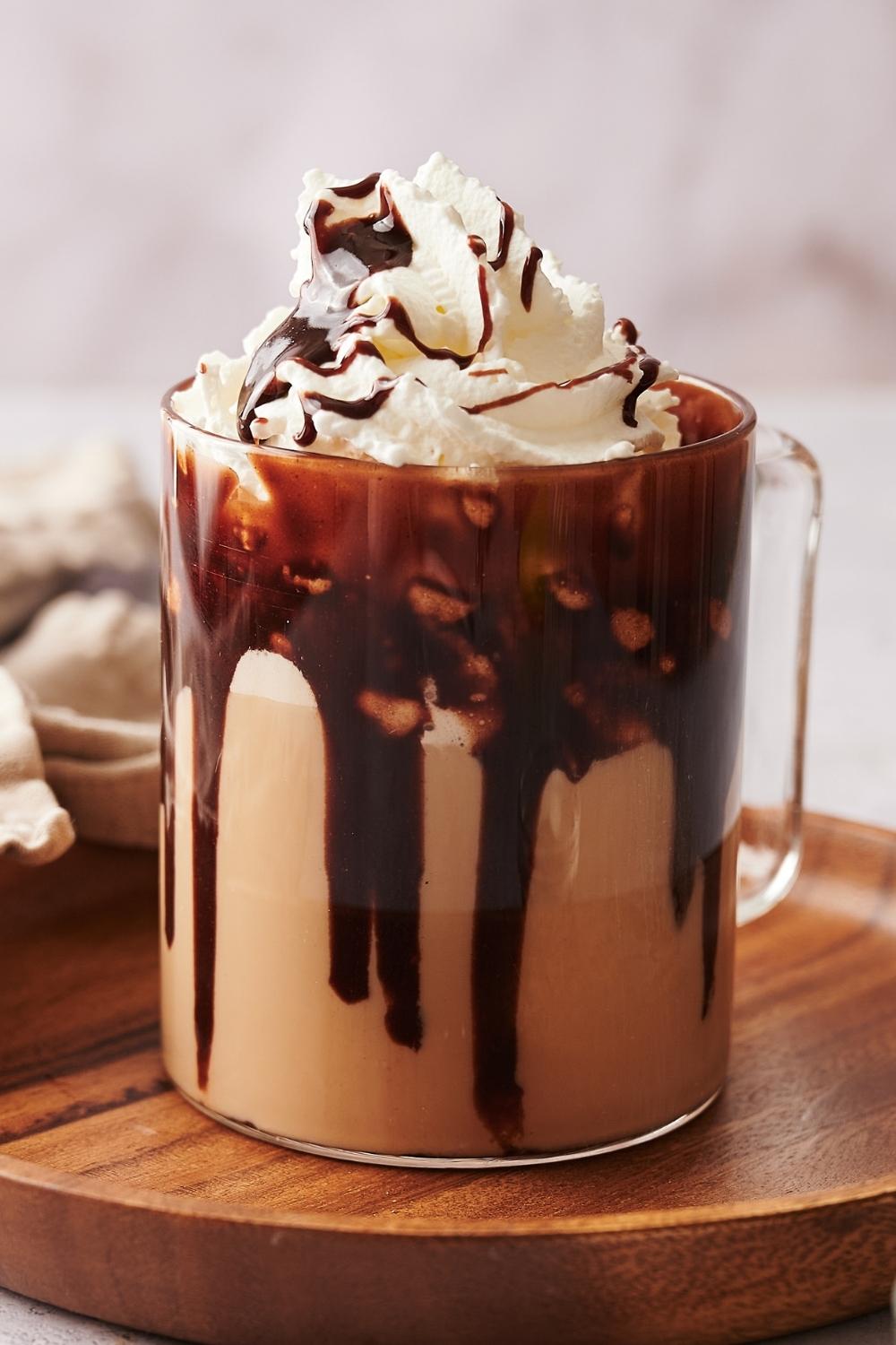 A clear glass mug with a homemade starbucks cafe mocha topped with whipped cream and chocolate syrup drizzled on top.