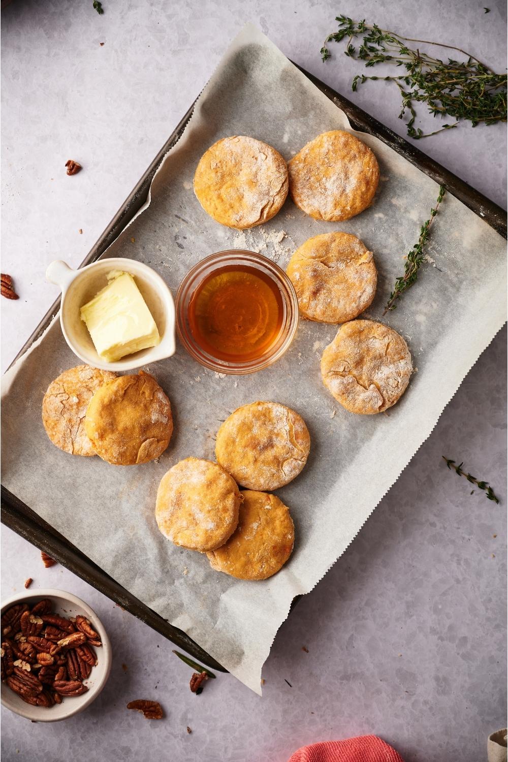 Sweet potato biscuits on a baking sheet lined with parchment paper next to bowls of butter and maple syrup.