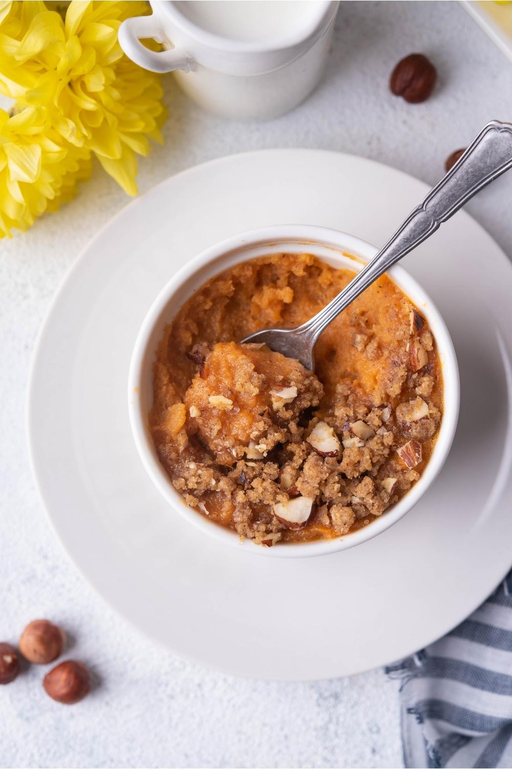 Partially eaten sweet potato souffle in a ramekin on a white plate with a spoon in the souffle.