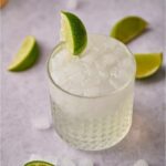 Texas ranch water in a highball glass garnished with a lime wedge and surrounded by lime wedges and ice cubes.