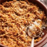 Poppy seed chicken casserole in a red casserole dish with a spoon in the dish.