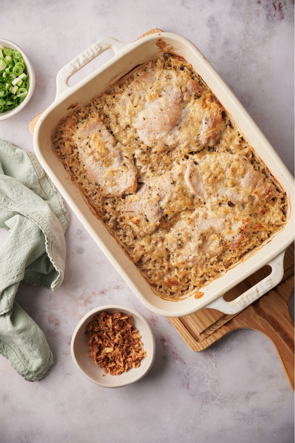 Cooked pork chop casserole in a white baking dish on top of a wood board.