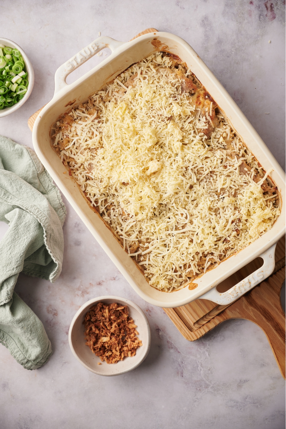 Shredded cheese covering a casserole in a white casserole dish that is on top of a wood board.