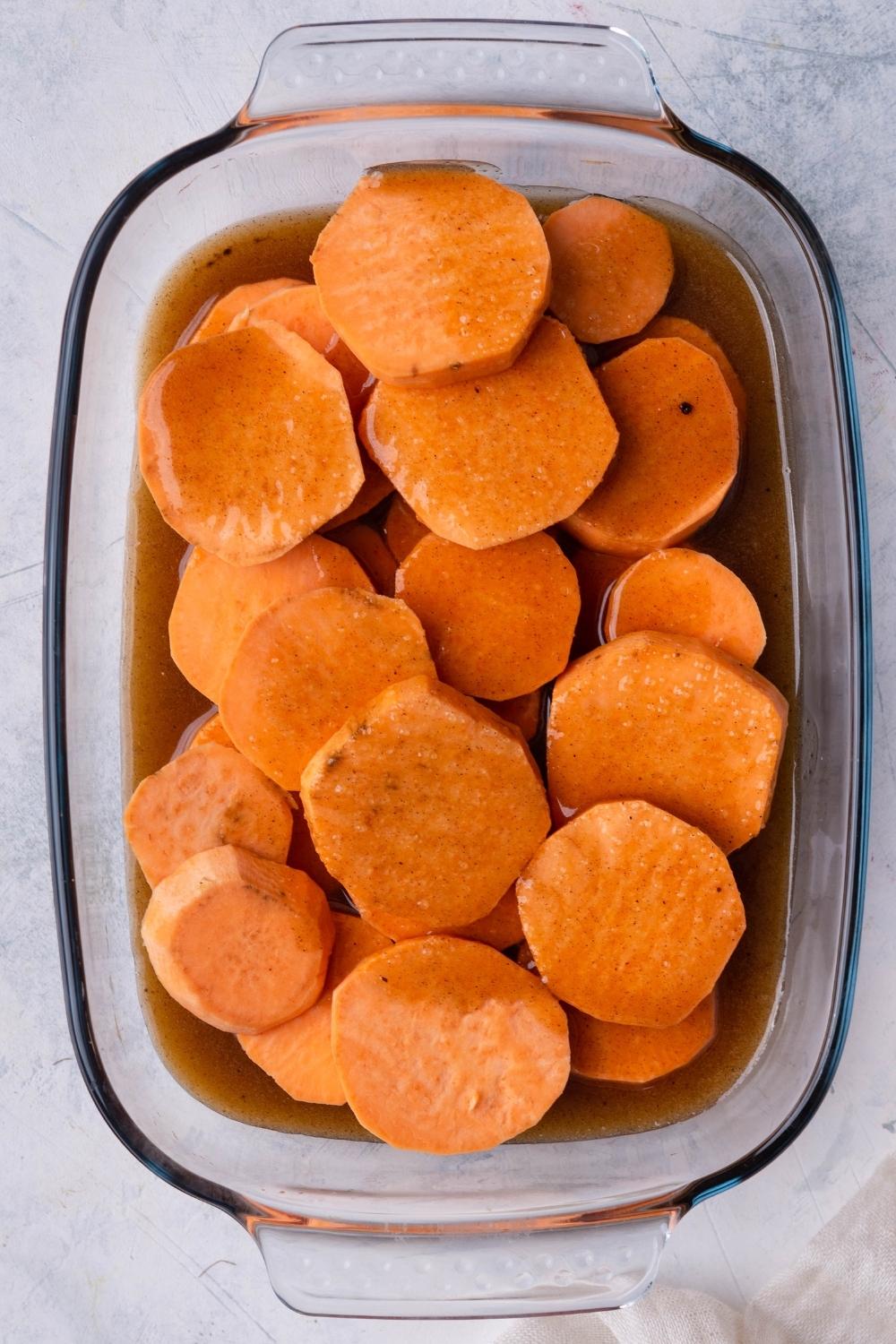 A baking dish with uncooked sliced sweet potatoes and the brown sugar mix.