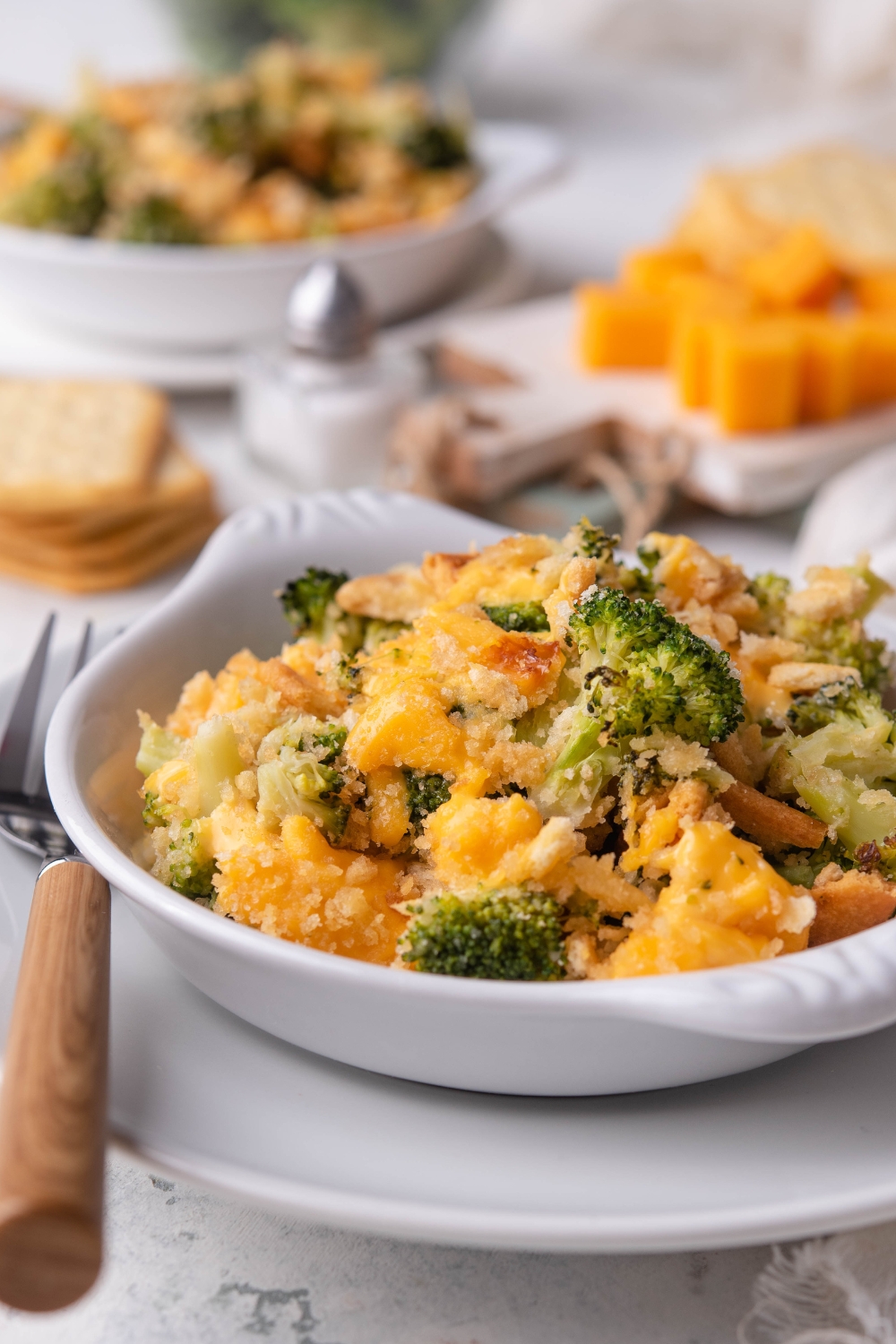 A dish containing cheddars broccoli cheese casserole. A fork sits next to it.