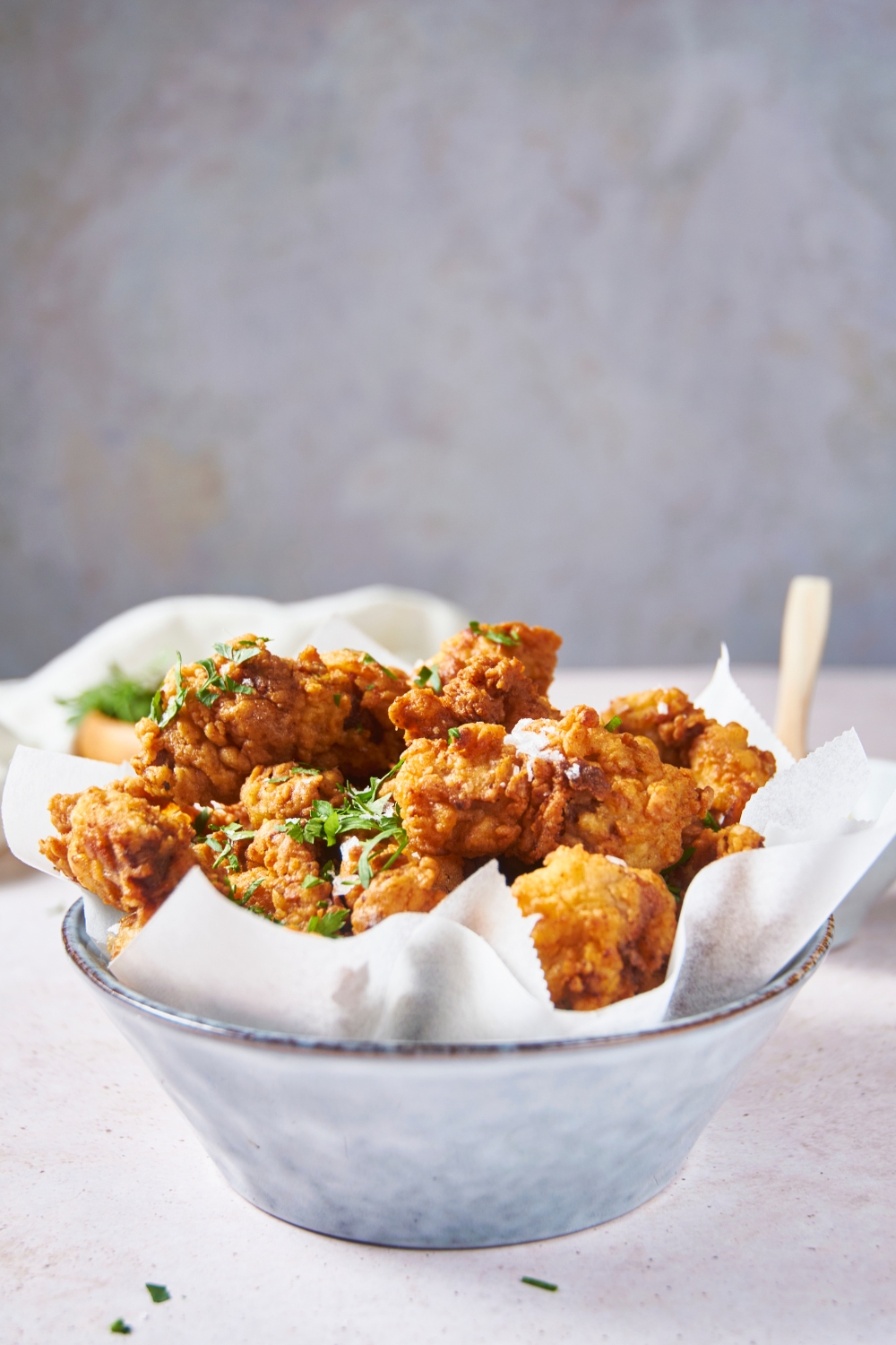 A blue bowl lined with parchment paper and filled with fried chicken pieces that have been garnished with fresh herbs.