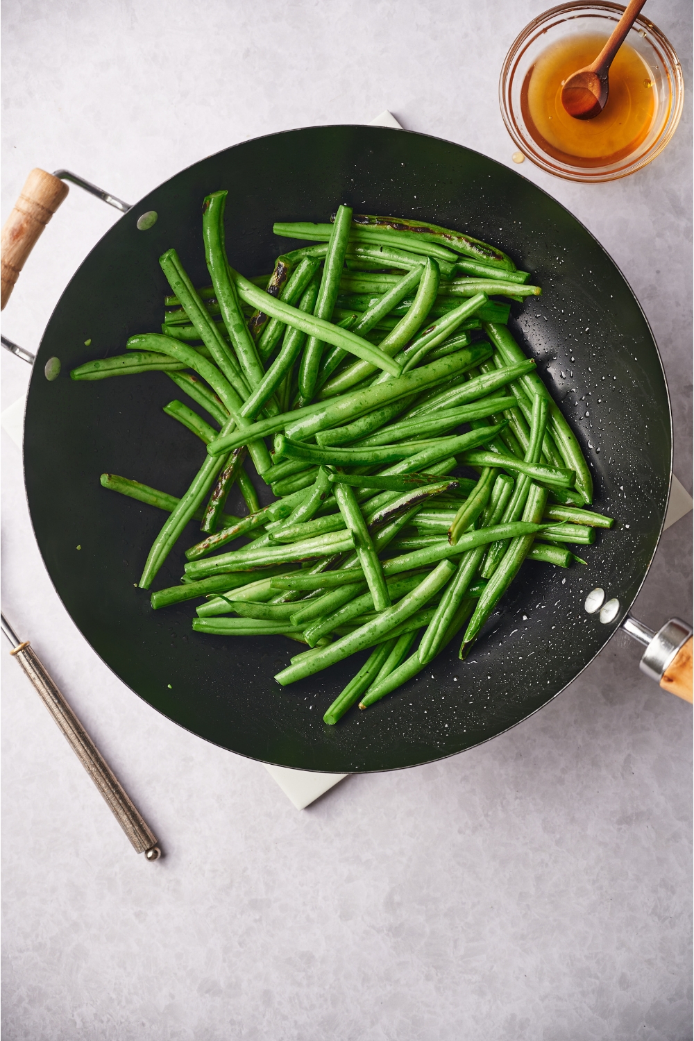 A black skillet with green beans. Next to the skillet is a small bowl of honey.