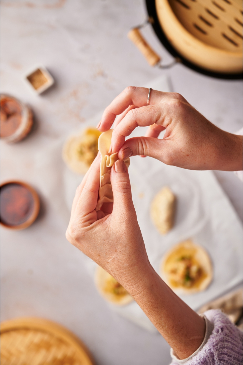 A hand pinching a dumpling to seal it. Below are more open-faced dumplings ready to be sealed.