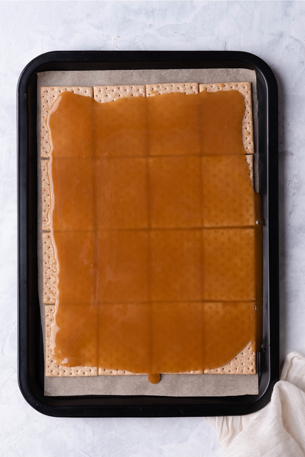 A baking sheet lined with parchment paper filled with saltine crackers covered in a caramel mixture.